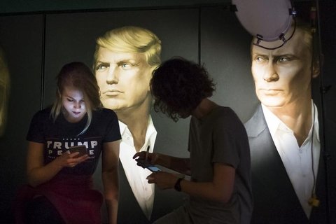 two people texting in front of images of a white man with blond hair.