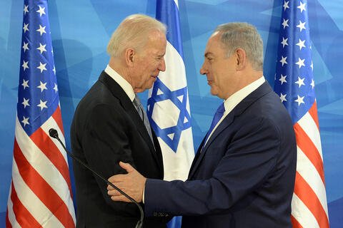 Two men in suits standing in front of the Israeli and US flags