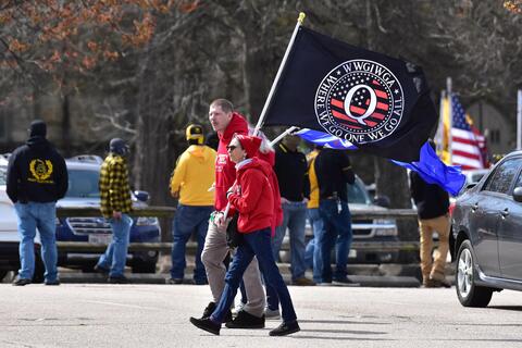 Two people in red hoodies carrying a QAnon flag