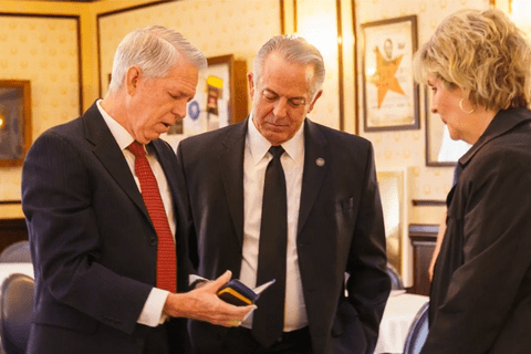 Two men looking into a book, and a woman looking at them