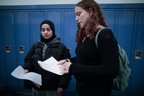 two girls with backpacks holding papers