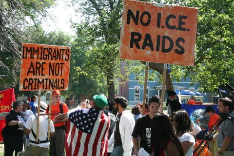 Protestors with signs saying "Immigrants are not criminals" and "No I.C.E. raids"