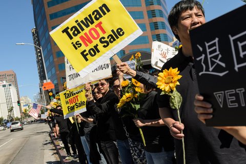 people standing in a row holding sunflowers. A sign says "Taiwan is not for sale."