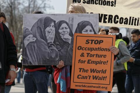 A person holding an image of women crying and a sign that says "stop occupations and torture for empire! The world can't wait!"