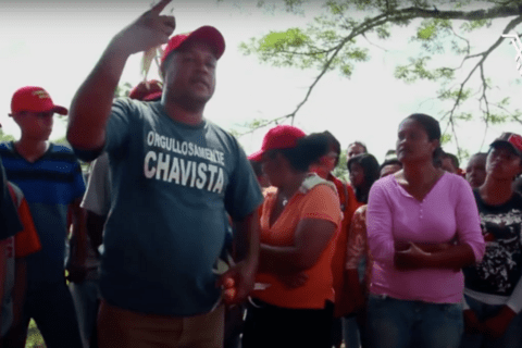 A group of people wearing red hats led by a man speaking with his hand raised. 