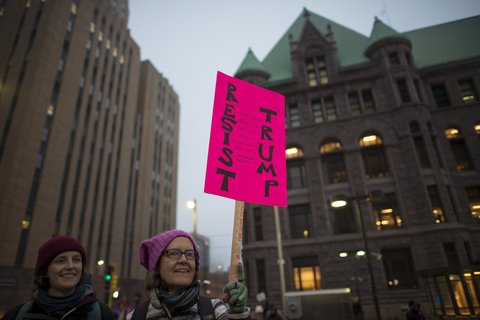 Woman holds a pink sign that reads "resist trump"