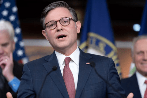 A man in a suit talking with people standing behind him.