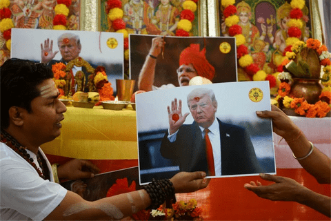 A man in religious outfit with a photo of Trump, performing a ceremony.