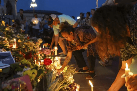 a wall of flowers and candles and people bending over to light them.
