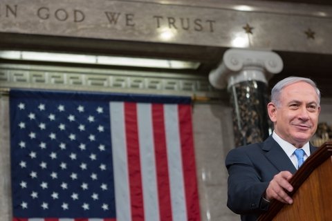 Benjamin Netanyahu smirks at a podium with American Flag behind him.