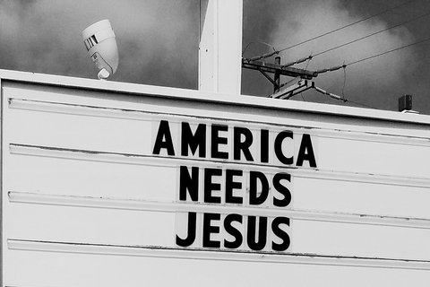 a black and white photo of a marquee sign reads "America needs jesus"