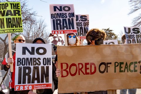 Antiwar protest signs that read "No bombs on Iran" and "Bored of Peace?"