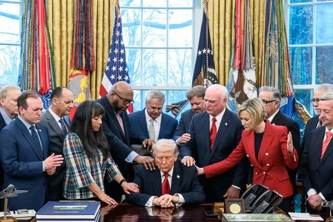 Trump in the center with people around him with they eyes closed, praying.