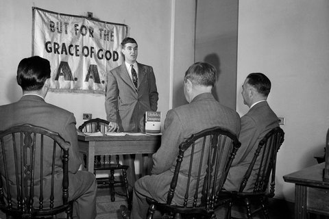 Black and white photo of men in suits with a banner on the wall "But for the grace of god"