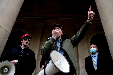 a man with a megaphone pointing, with two men in the background