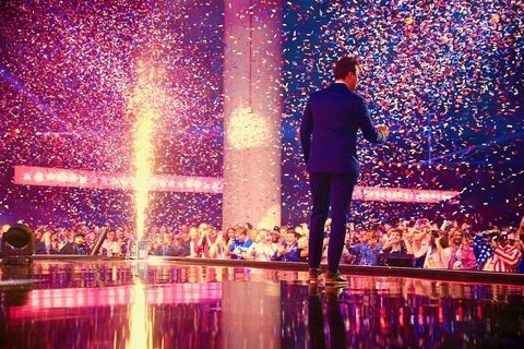 the back of a man standing on a stage with pyrotechnics around him.