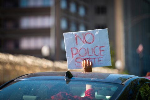 A person holding a sign out of a sun roof that reads "no police state"