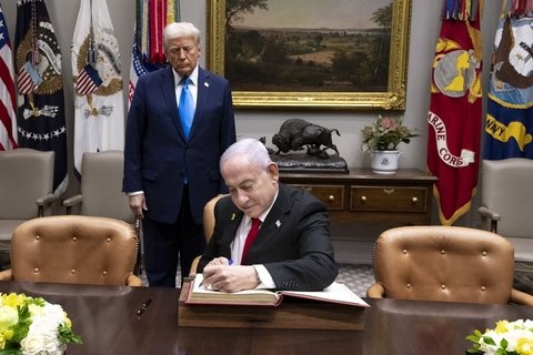 donald trump in blue suit stands behind seated benjamin netanyahu signing a document