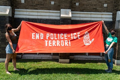 two people holding a banner that reads "End Police-ICE Terror" with a palm with 287g on it.
