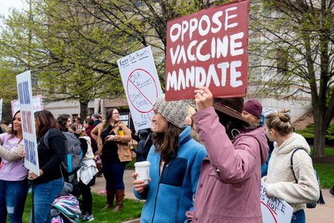 a protestor holding a sign that says "Oppose Vaccine Mandate"