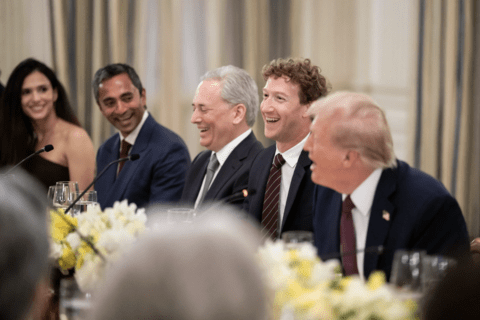 A woman sits next to four men in suits laughing together at a White House discussion 
