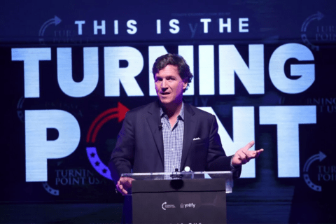 a man in a suit standing at a podium with "this is the turning point" behind him
