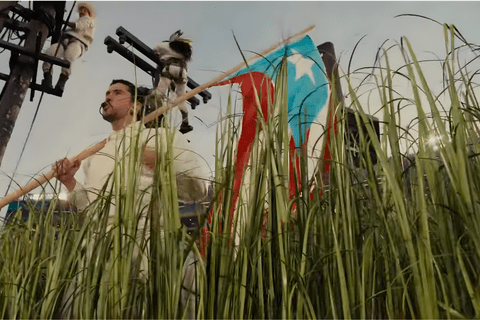 Bad Bunny stands in front of electrical poles waving the Puerto Rican independence flag