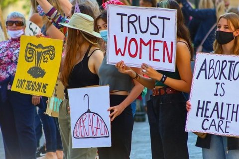 Feminine adults holding protest signs including "Trust Women."