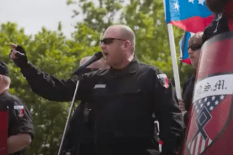 A blad man in sunglasses talking into a mic
