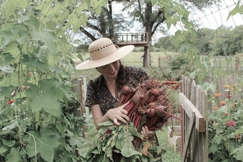 a woman in a straw hat and dress picks radishes in a bucolic setting