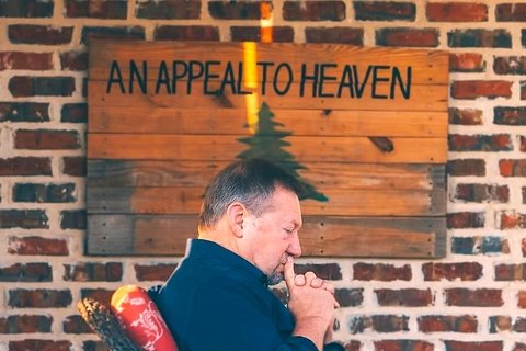 Side view of Apostle Dutch Sheets posing thoughtfully against a wooden sign that reads "An Appeal to Heaven"