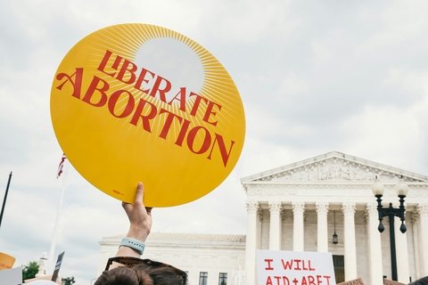 Protest photo featuring round yellow sign that reads "Liberate Abortion" in red text