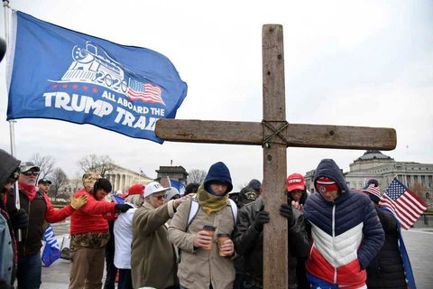 Participants in the January 6 insurrection hold a giant wooden cross and pray