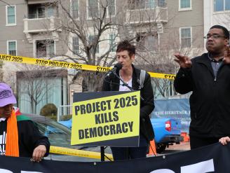 Two people on a podium with a board that reads "Project 2025 Kills Democracy"