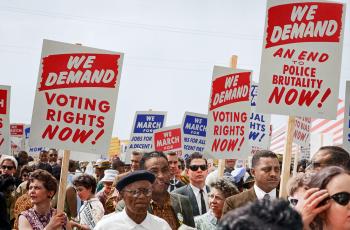 People at a protest holding a sign that says "We Demand Voting rights now!" "We demand An end to police brutality now"