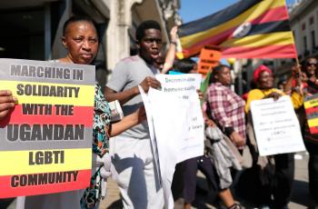 A woman in the front of the frame holding a sign that reads "marching in solidarity with the Ugandan LGBTI Community"