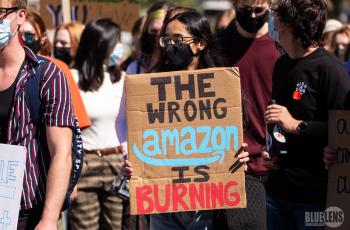 A person wearing a mask holding a sign saying "The wrong Amazon is burning"