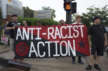 People holding a red and black flag that reads Anti-Racist Action