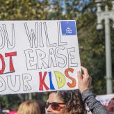 Hands holding up sign reading "You will not erase our kids"