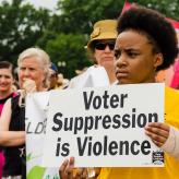 A Black person in a yellow T-shirt holding a sign that says "voter suppression is violence"