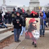 A woman in front of the U.S. Capitol building, wearing a red hat, holding an image of Jesus wearing a Make America Great Again hat, and WWG1WGA on his shirt