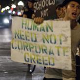 A person carrying a sign that reads "Human need not corporate greed"