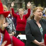 Older woman standing in crowd with both hands raised