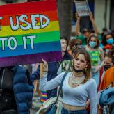 A woman at a Pride march in Paris holding a sign painting in the LGBT colors that says "Get used to it"