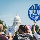A protester in front of the Capitol holding a sign that says "Keep Abortion Legal"