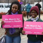 Three women holding signs that say "We march for Woomen's Health."