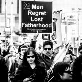 A man wearing sunglasses holding a sign that says "Men Regret Lost Fatherhood"