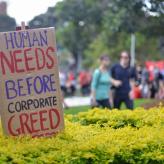 A cardboard sign that says Human Needs Before Corporate Greed
