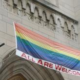 A rainbow flag outside a church with the words "All are welcome"