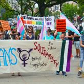 Protesters holding a banner that says Trans Solidarity against transphobia.